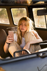 Young woman sitting in a van using cell phone