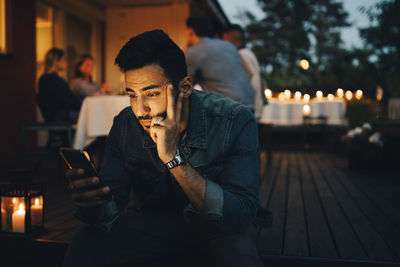 Man using mobile phone while friends in background during dinner party