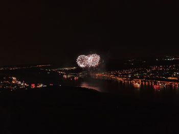 Firework display over illuminated city against sky at night