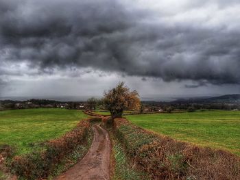 Dirt road amidst field against storm clouds