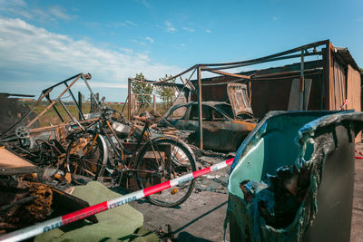 Abandoned bicycle with garbage can at junkyard against sky