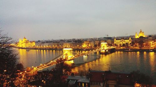 Illuminated bridge over river with city in background