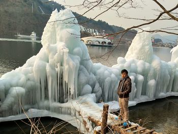 Man standing on footbridge by ice formation over lake