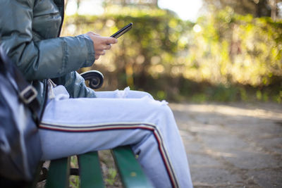 Midsection of woman holding smart phone while sitting outdoors