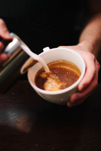 Close-up of hand pouring cream in coffee cup