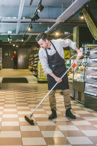 Full length of salesman sweeping floor in grocery store