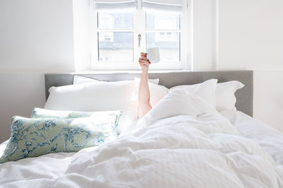 Low section of woman sleeping on bed at home - coffee cup in the air