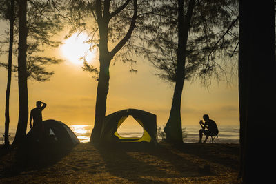 Silhouette camping tent with people relax on beach with sunrise and sea background