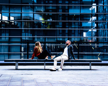 Full length of couple sitting on building in city