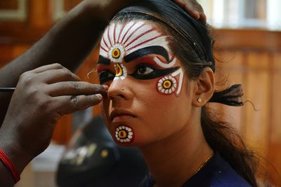 Cropped hand applying make-up on woman during carnival