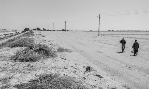 People walking on snow covered landscape against clear sky