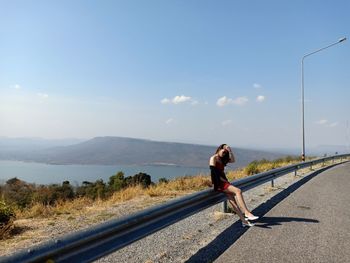 Young woman sitting on railing by road