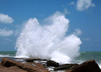 Waves splashing on rocks against sky