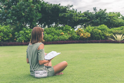 Rear view of woman reading book on field