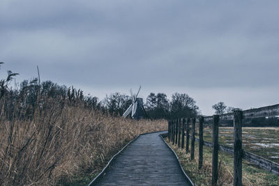 Footpath amidst trees on field against sky