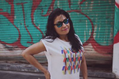 Young woman wearing sunglasses standing against graffiti wall