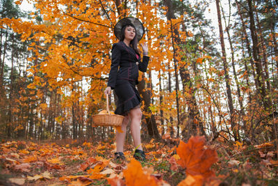 Full length of woman with autumn leaves in forest