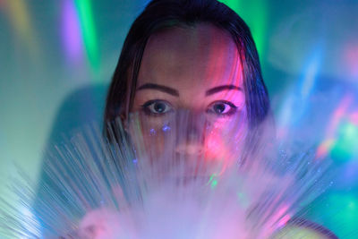 Close-up portrait of young woman holding illuminated fiber optic against wall