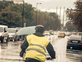 Rear view of man in reflective clothing cycling on wet city street