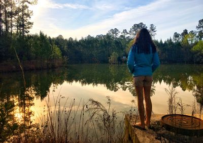 Rear view of woman standing by lake against sky