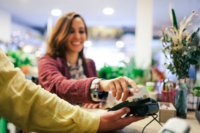 Smiling woman paying through credit card while standing with buyer at cash counter