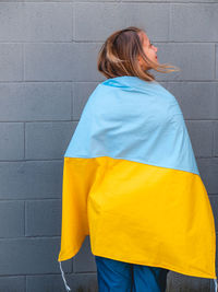 Caucasian blond teenager wrapped in an ukrainian flag over a neutral background 