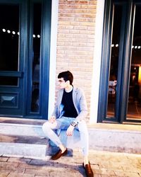 Young woman sitting on window of building