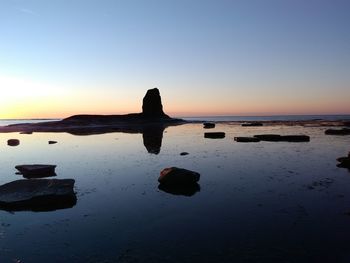 Silhouette rock on beach against clear sky at sunset