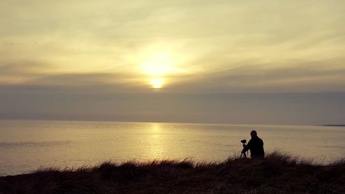 Silhouette man and dog standing on beach against sky during sunset