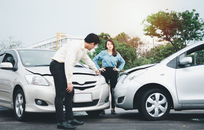 People standing by car on road against trees