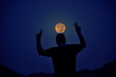 Silhouette man gesturing peace sign against moon at night
