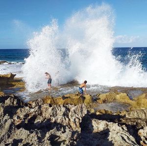 Waves splashing on rocks at shore against sky