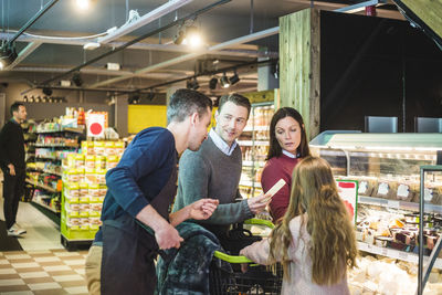 Man holding product while talking to sales clerk by family in supermarket