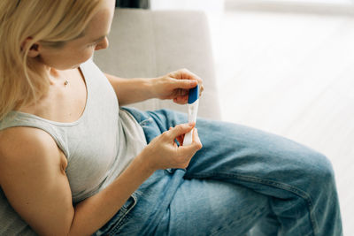 A woman is holding a pregnancy test in her hands and waiting for the result sitting on the couch.