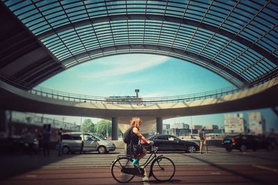 Woman riding bicycle on bridge in city