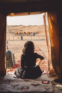 Rear view of woman sitting on blanket at sahara desert seen through tent