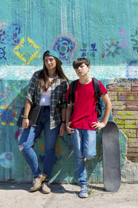 Full length portrait of students standing against painted wall during sunny day