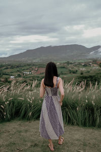 Rear view of woman standing on field against sky