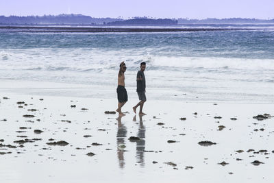 Full length of friends showing thumbs up sign at beach