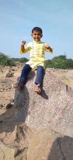 Portrait of cute boy sitting on rock against clear sky