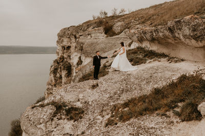 Rear view of woman standing on rock by sea against sky