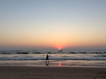 Rear view of man standing at sea shore against clear sky during sunset