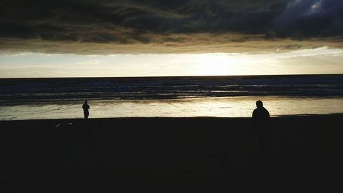 Silhouette people standing on beach at sunset