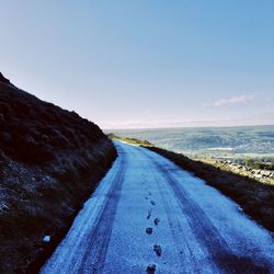 Empty road by sea against sky