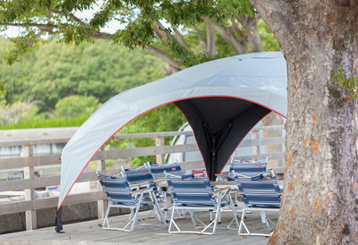 Tarp shelter, folding chairs and table under a tree in camping ground