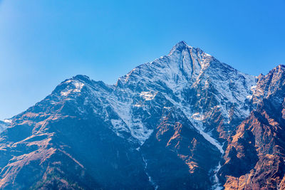 Low angle view of snowcapped mountains against clear blue sky