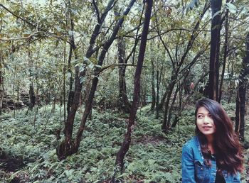 Smiling young woman standing against trees at forest