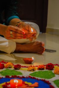 Low section of woman holding diya while sitting on tiled floor at home