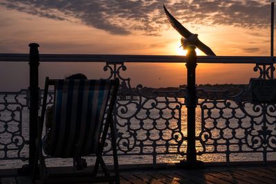Person sitting on chair at pier against sea during sunset