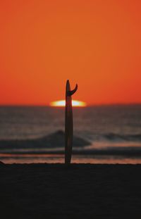 Silhouette surfboard at beach against sky during sunset